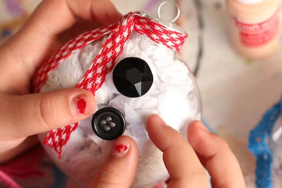 kid gluing buttons on snowman belly ornament with red checkered scarf
