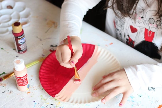 kid painting santa hat and face on paper plate