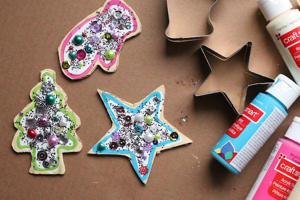 Decorated star, mitt and christmas tree ornaments on piece of cardboard with paint and cookie cutters