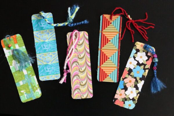 5 homemade fabric bookmarks with colourful yarn tassels on black background