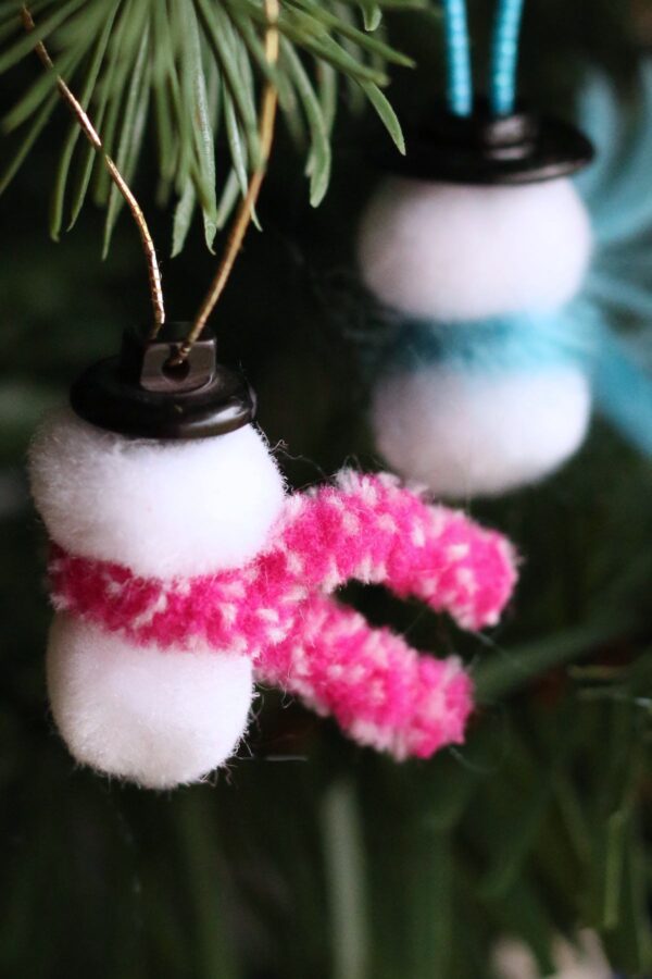 2 small pom pom snowmen one with pink scarf, one with blue scarf, hanging on Christmas tree
