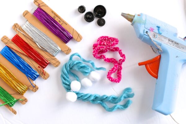 metallic thread, blue yarn, pink yarn, white pom poms, black buttons, glue gun
